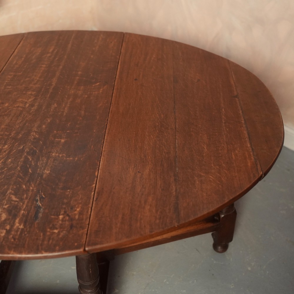 An 18th-century Georgian oak gateleg dining table featuring a round drop-leaf top, turned legs, and stretchers in a dark brown finish. View VII