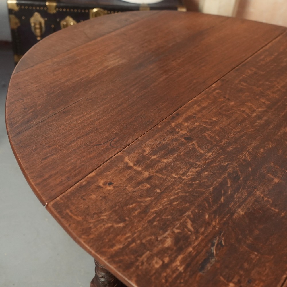 An 18th-century Georgian oak gateleg dining table featuring a round drop-leaf top, turned legs, and stretchers in a dark brown finish. View VIII