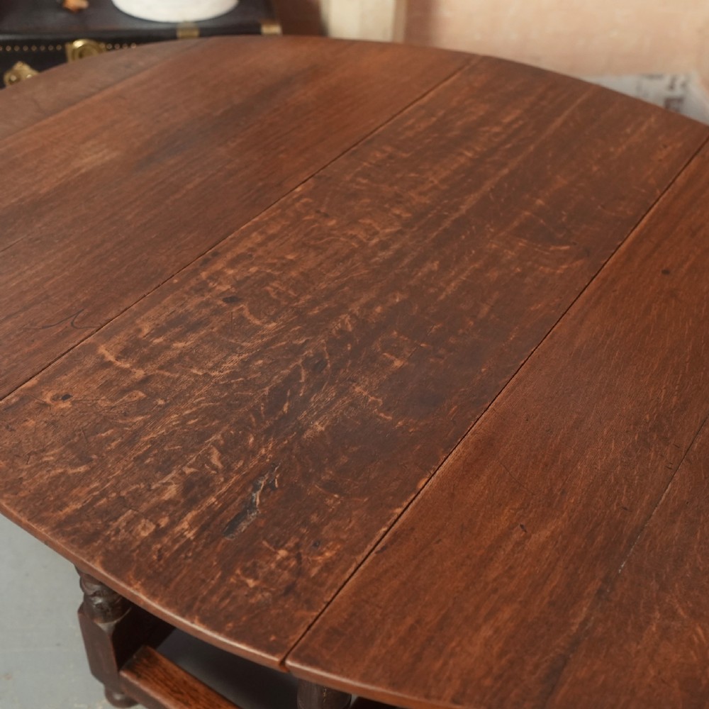 An 18th-century Georgian oak gateleg dining table featuring a round drop-leaf top, turned legs, and stretchers in a dark brown finish. View IX