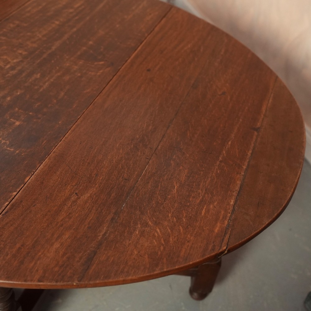 An 18th-century Georgian oak gateleg dining table featuring a round drop-leaf top, turned legs, and stretchers in a dark brown finish. View X