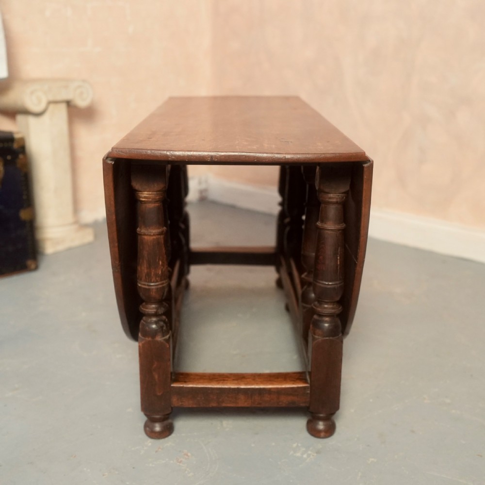 An 18th-century Georgian oak gateleg dining table featuring a round drop-leaf top, turned legs, and stretchers in a dark brown finish. View XI