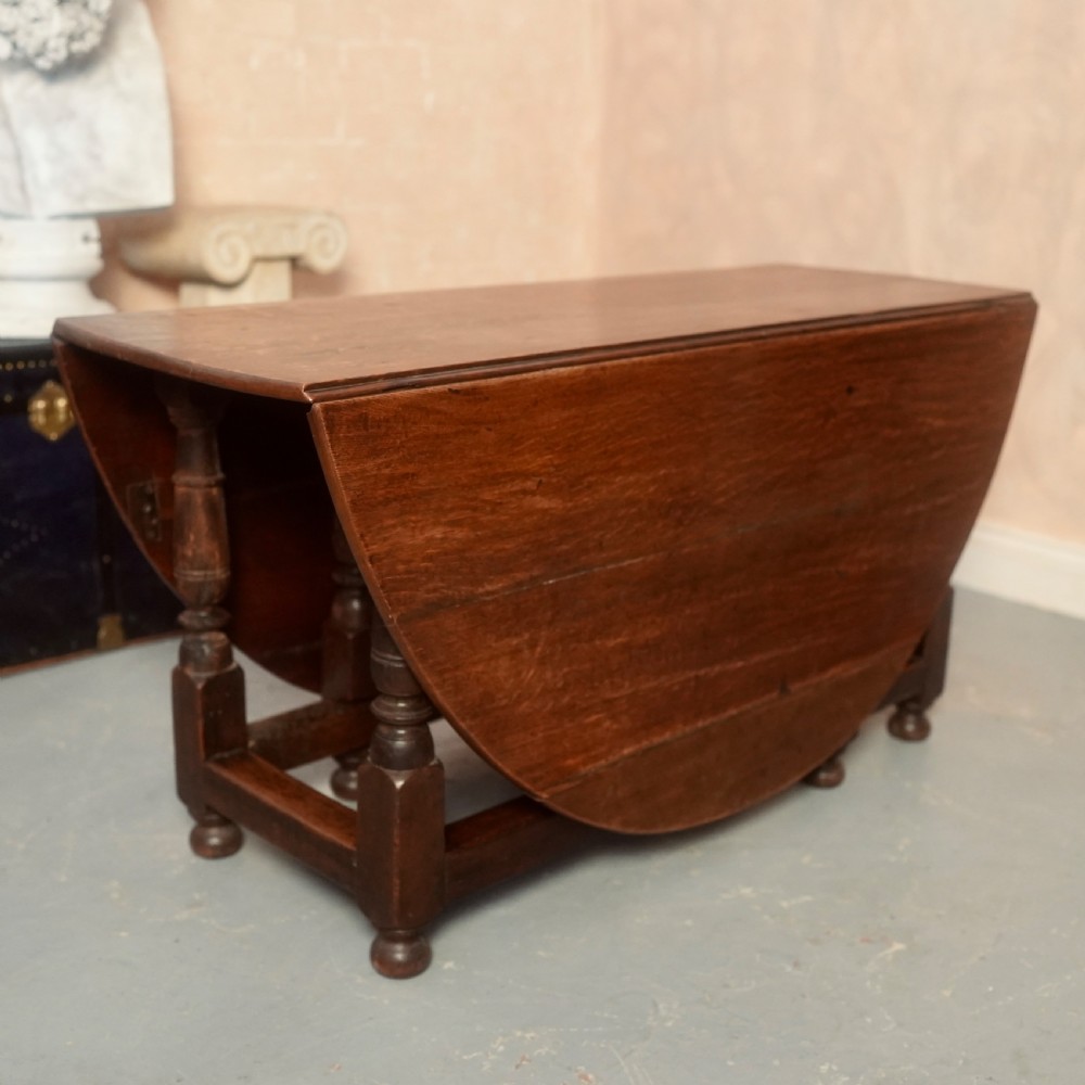 An 18th-century Georgian oak gateleg dining table featuring a round drop-leaf top, turned legs, and stretchers in a dark brown finish. View XII