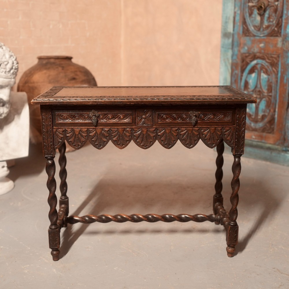 A 19th-century dark carved oak writing table featuring barley twist legs, a scalloped apron frieze, and twin drawers with ornate metal pulls.