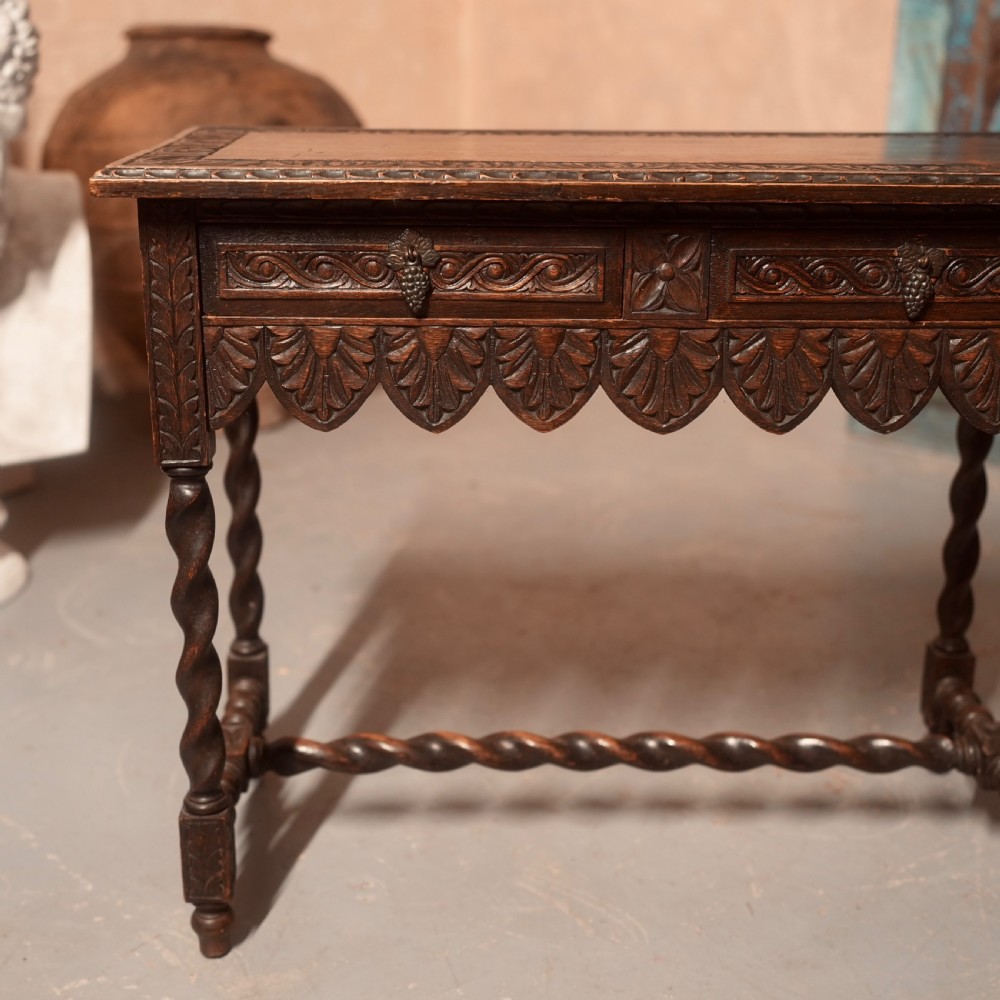 A 19th-century dark carved oak writing table featuring barley twist legs, a scalloped apron frieze, and twin drawers with ornate metal pulls. View II
