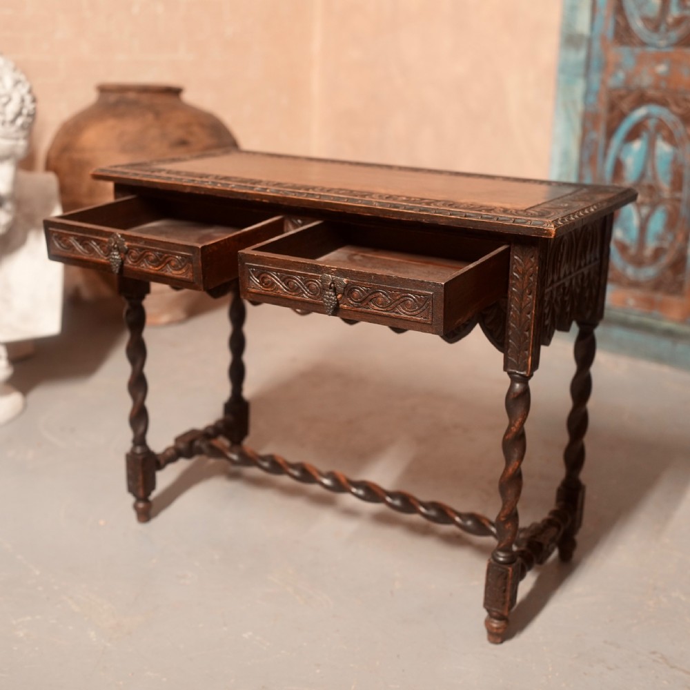 A 19th-century dark carved oak writing table featuring barley twist legs, a scalloped apron frieze, and twin drawers with ornate metal pulls. View V