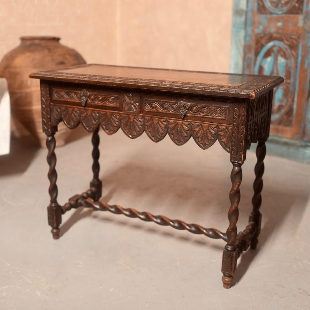 A 19th-century dark carved oak writing table featuring barley twist legs, a scalloped apron frieze, and twin drawers with ornate metal pulls. View VI