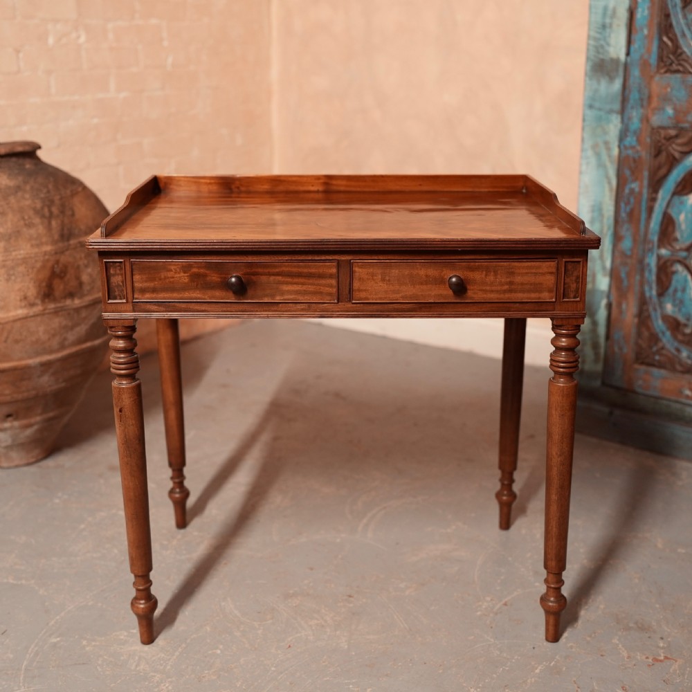A Georgian mahogany writing table featuring a low gallery rim, two frieze drawers with turned wooden knobs, and slender turned legs.