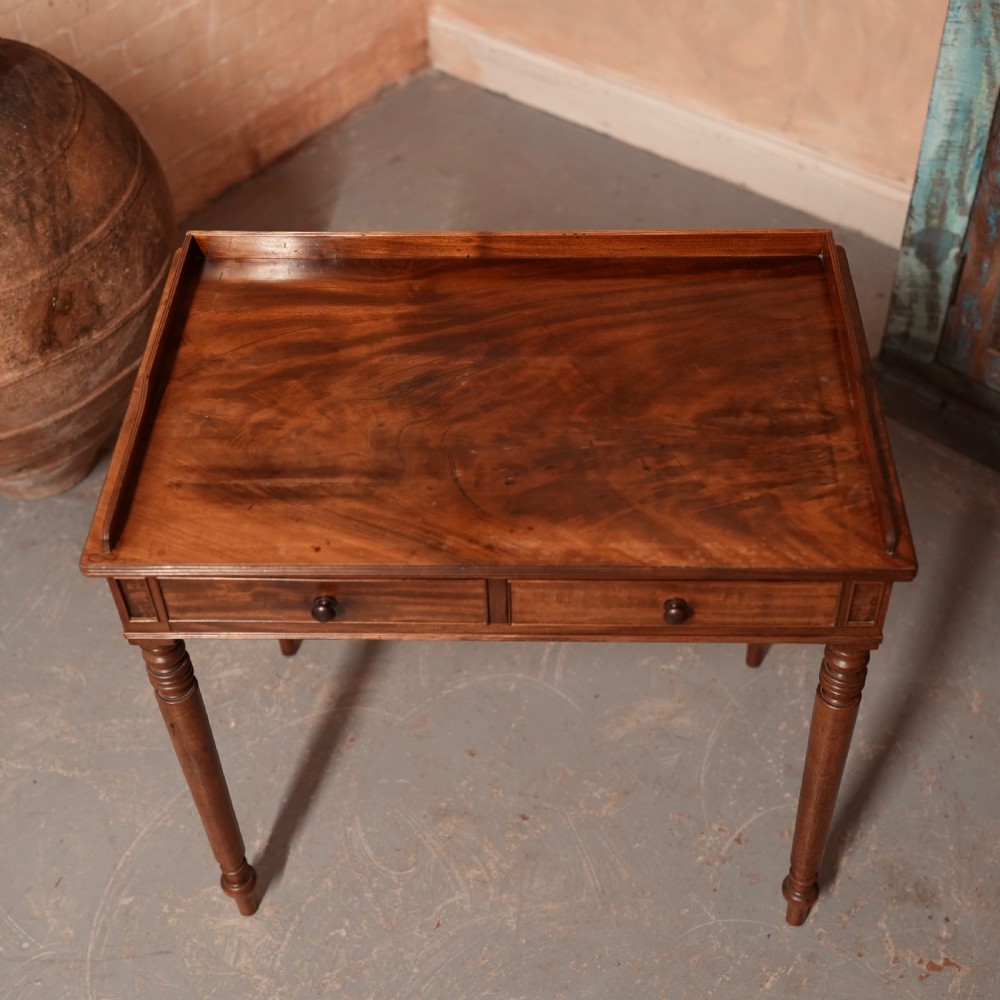 A Georgian mahogany writing table featuring a low gallery rim, two frieze drawers with turned wooden knobs, and slender turned legs. View V