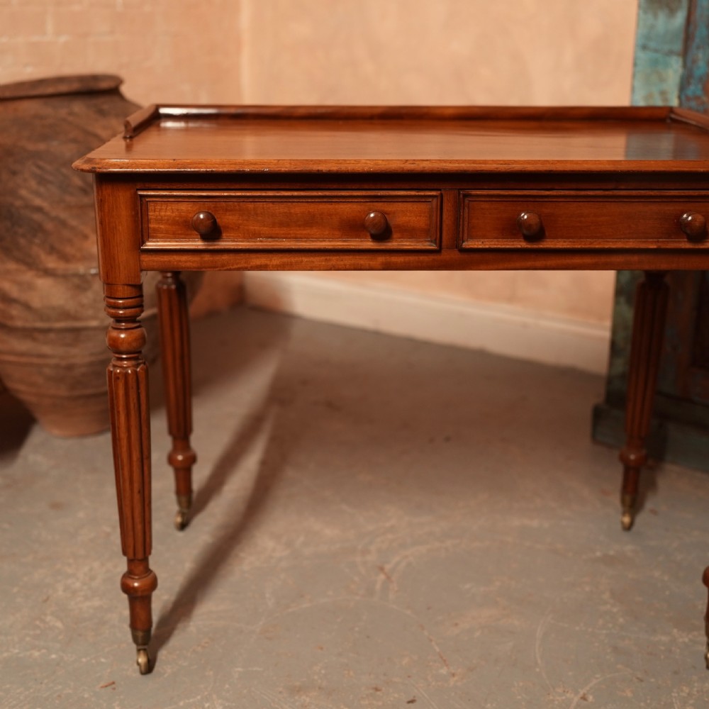 A William IV mahogany writing table featuring a raised gallery top, two frieze drawers with wooden knob handles, and reeded turned legs with brass castors. View XI