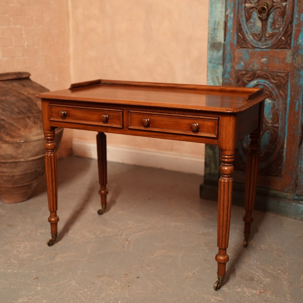 A William IV mahogany writing table featuring a raised gallery top, two frieze drawers with wooden knob handles, and reeded turned legs with brass castors. View II