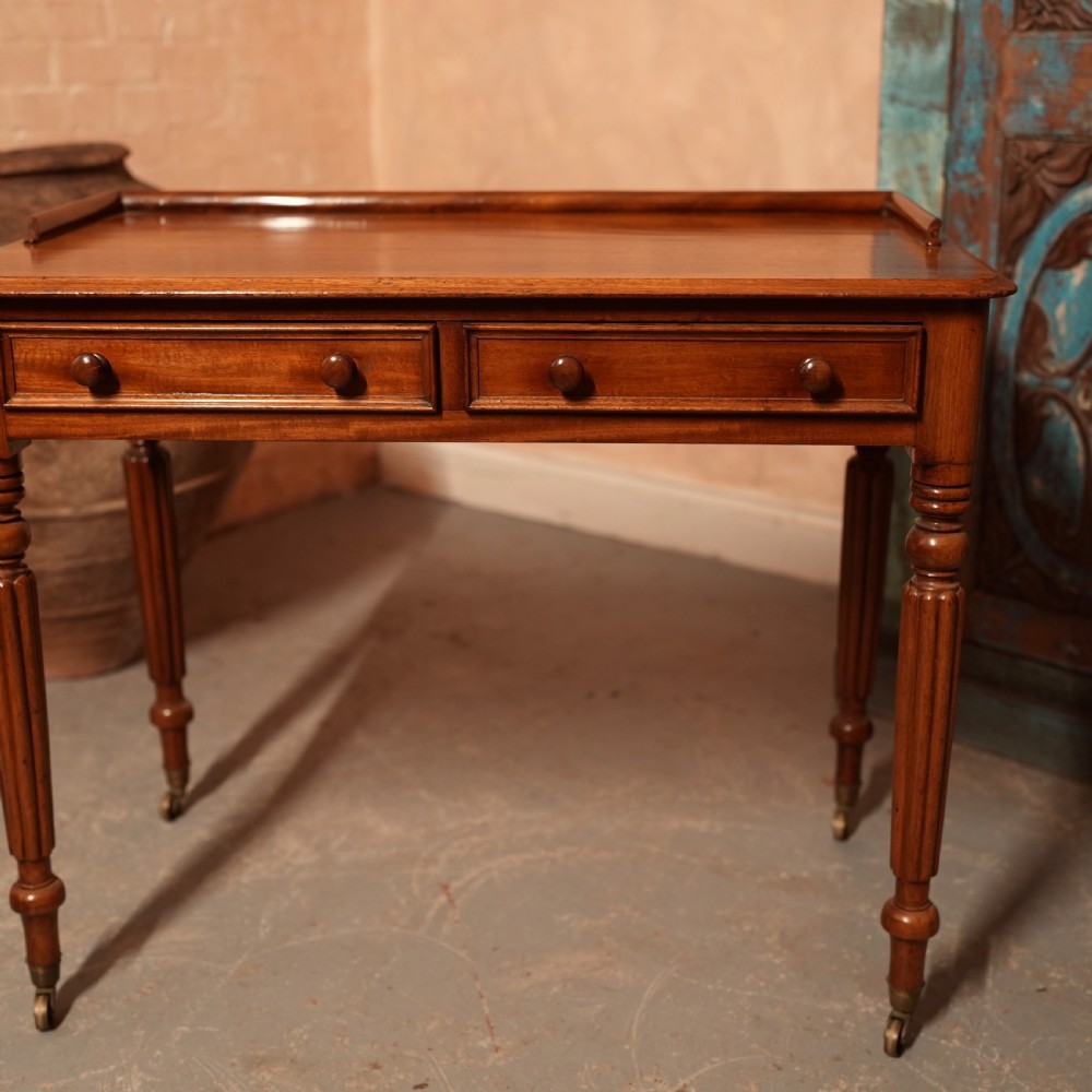 A William IV mahogany writing table featuring a raised gallery top, two frieze drawers with wooden knob handles, and reeded turned legs with brass castors. View IV