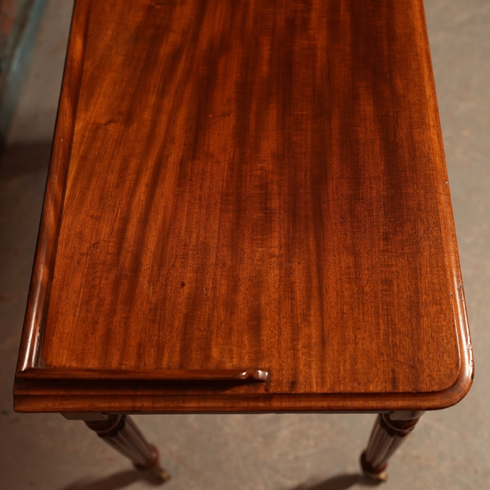 A William IV mahogany writing table featuring a raised gallery top, two frieze drawers with wooden knob handles, and reeded turned legs with brass castors. View V