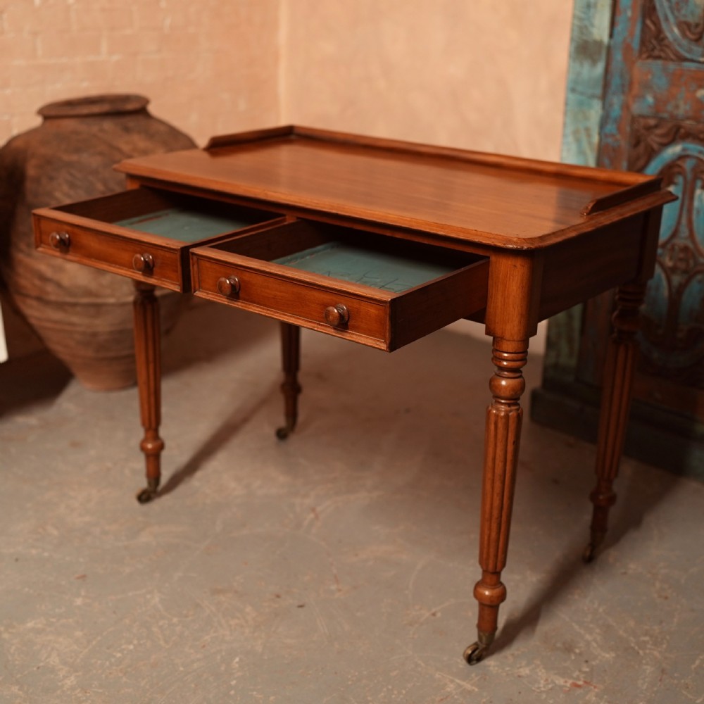 A William IV mahogany writing table featuring a raised gallery top, two frieze drawers with wooden knob handles, and reeded turned legs with brass castors. View IX