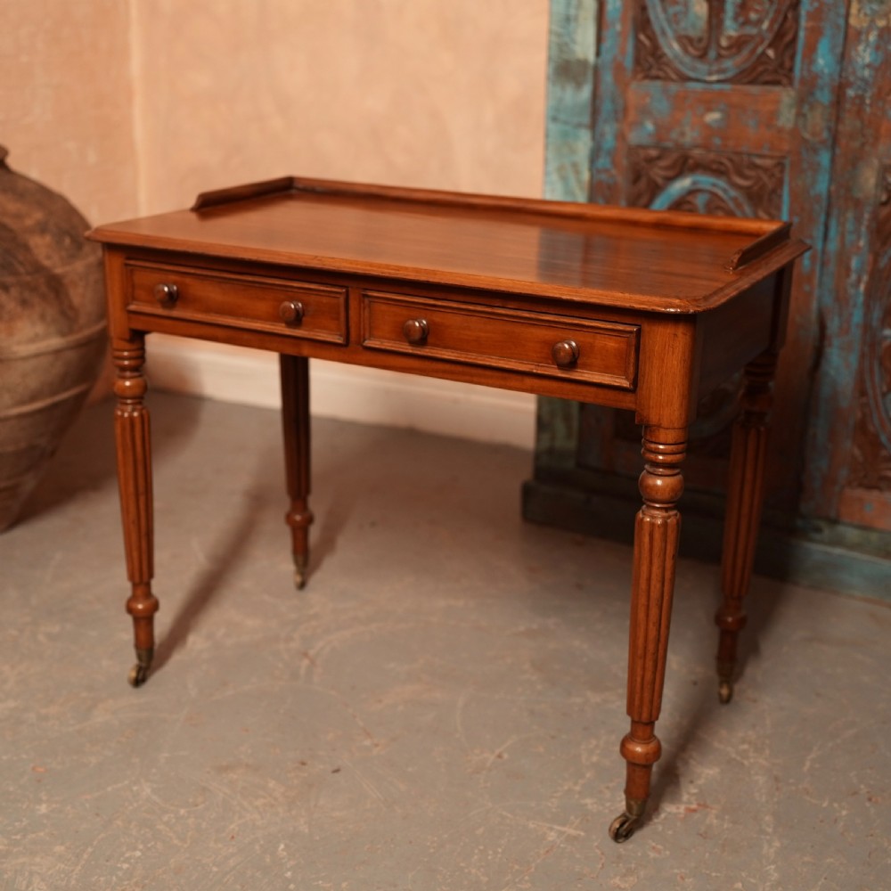 A William IV mahogany writing table featuring a raised gallery top, two frieze drawers with wooden knob handles, and reeded turned legs with brass castors.