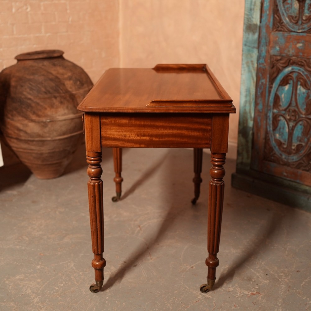 A William IV mahogany writing table featuring a raised gallery top, two frieze drawers with wooden knob handles, and reeded turned legs with brass castors. View XII