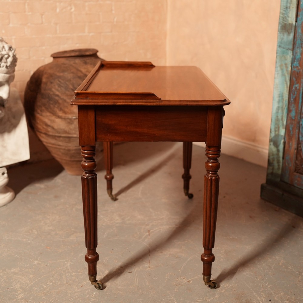 A William IV mahogany writing table featuring a raised gallery top, two frieze drawers with wooden knob handles, and reeded turned legs with brass castors. View XIV