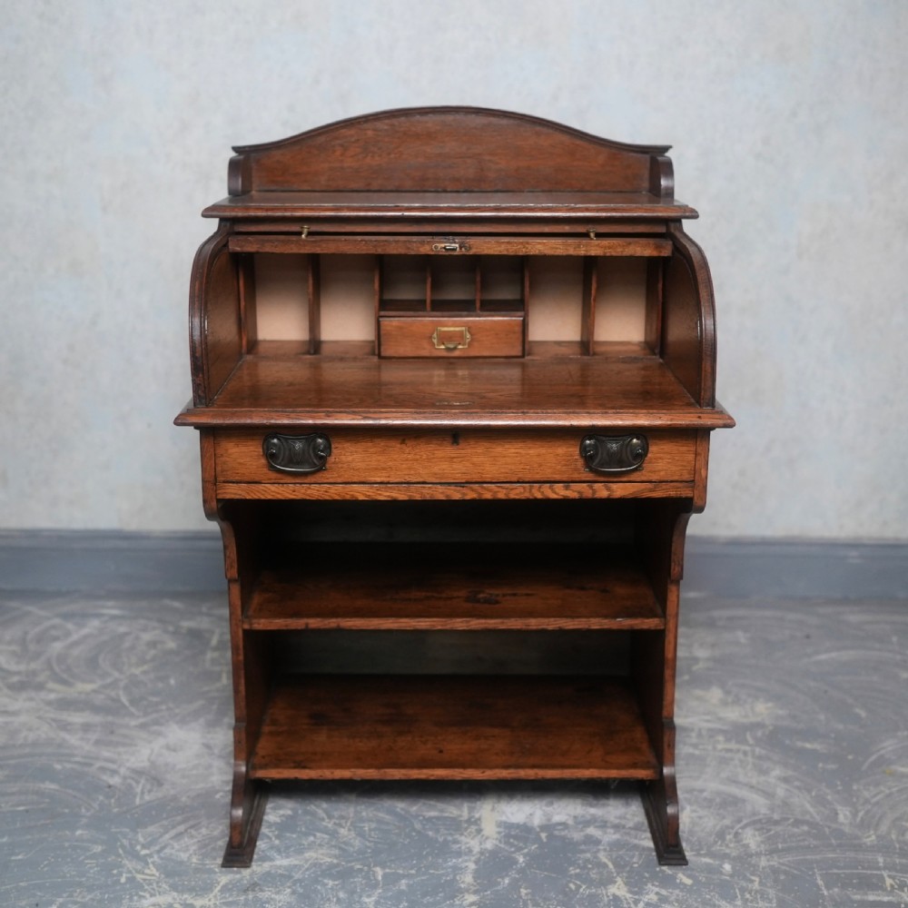 An Edwardian oak rolltop writing bureau featuring a tambour slatted shutter, a single frieze drawer with dark metal handles, an arched top gallery, and two open lower shelves. View II