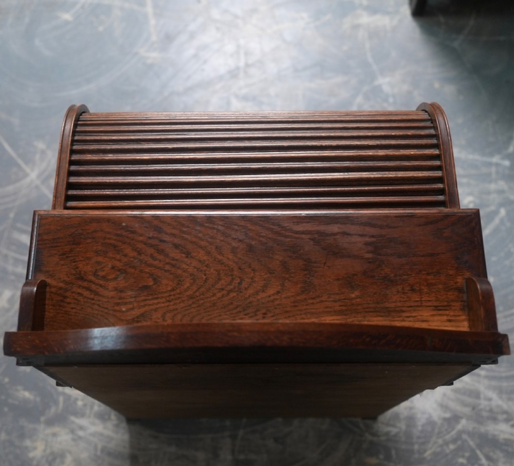 An Edwardian oak rolltop writing bureau featuring a tambour slatted shutter, a single frieze drawer with dark metal handles, an arched top gallery, and two open lower shelves. View III