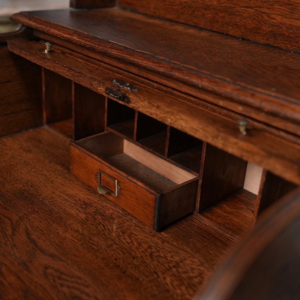An Edwardian oak rolltop writing bureau featuring a tambour slatted shutter, a single frieze drawer with dark metal handles, an arched top gallery, and two open lower shelves. View V