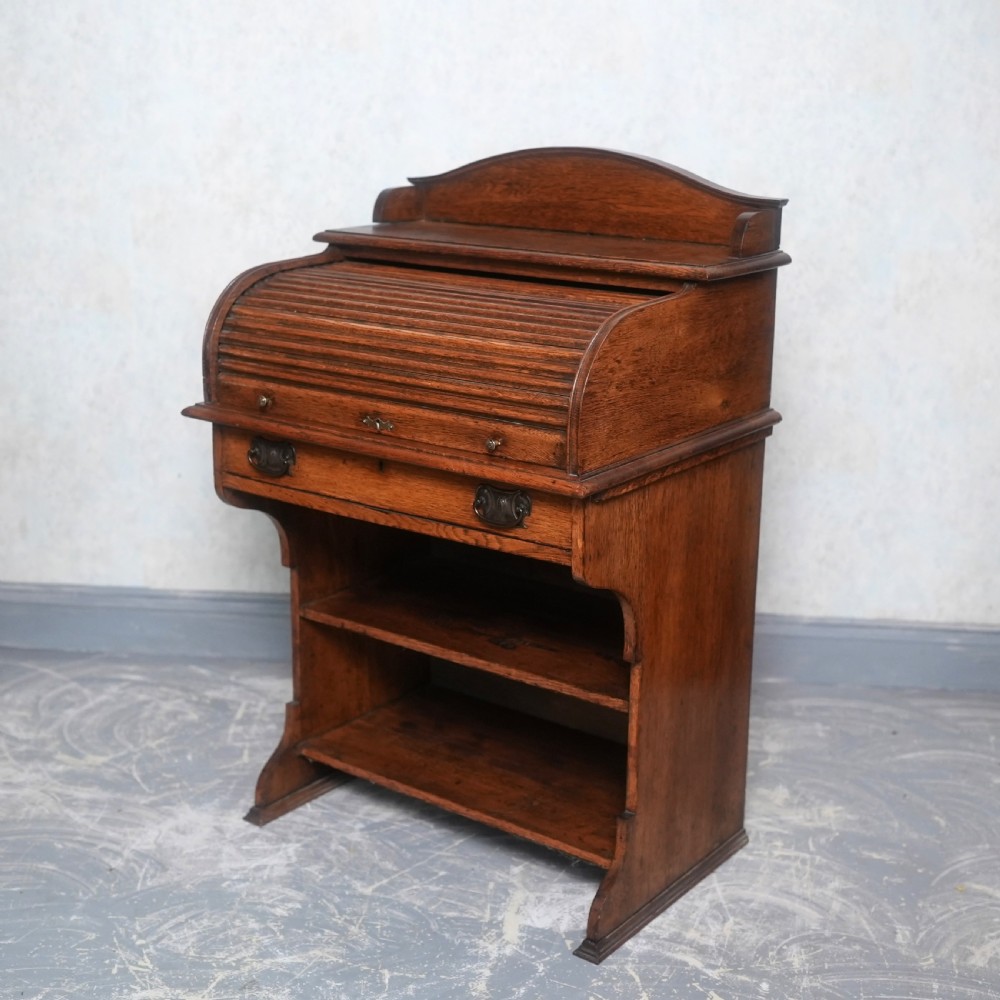 An Edwardian oak rolltop writing bureau featuring a tambour slatted shutter, a single frieze drawer with dark metal handles, an arched top gallery, and two open lower shelves. View VI