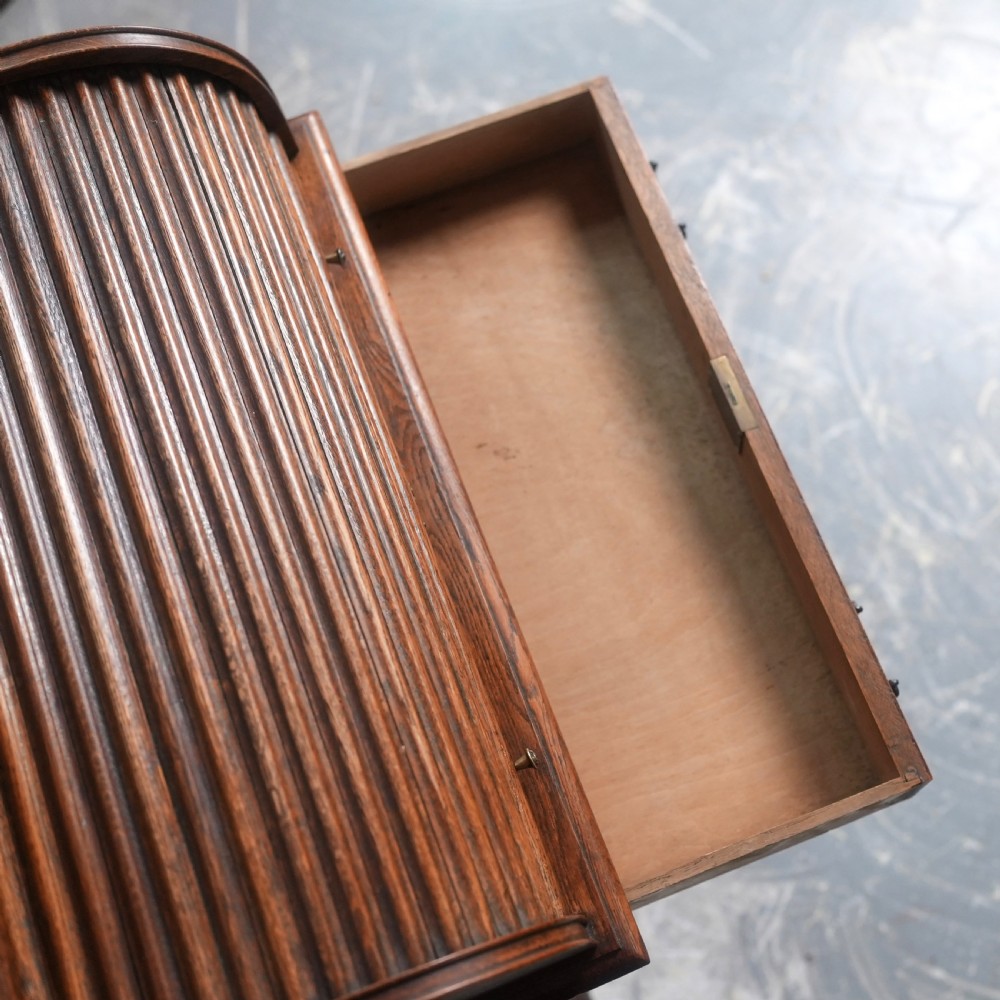 An Edwardian oak rolltop writing bureau featuring a tambour slatted shutter, a single frieze drawer with dark metal handles, an arched top gallery, and two open lower shelves. View VII