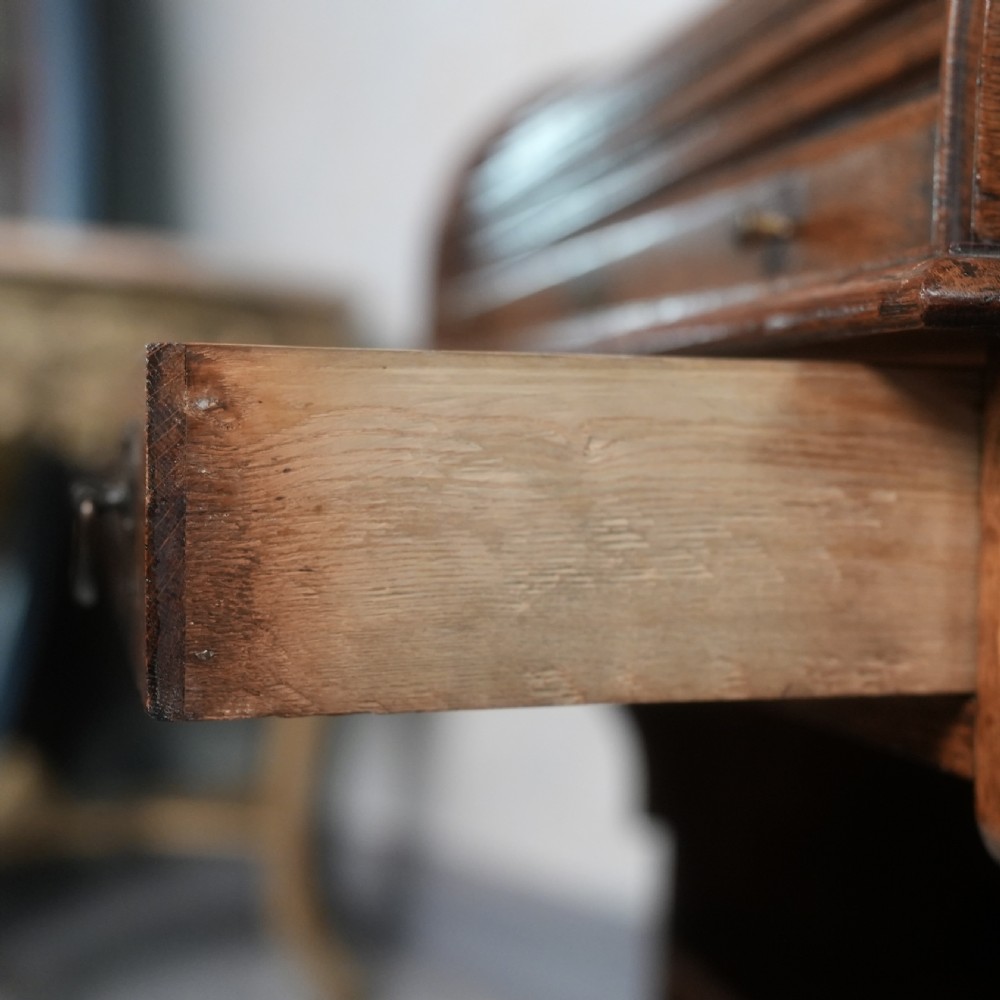 An Edwardian oak rolltop writing bureau featuring a tambour slatted shutter, a single frieze drawer with dark metal handles, an arched top gallery, and two open lower shelves. View VIII