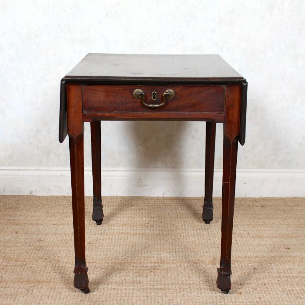 A Georgian mahogany drop leaf writing table featuring a single drawer with a brass handle, tapered legs, and side flaps.