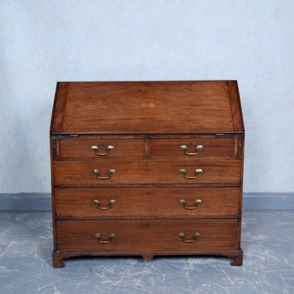 An antique Georgian mahogany writing bureau featuring a slanted fall-front top, four graduated drawers with brass swan-neck handles, and bracket feet.
