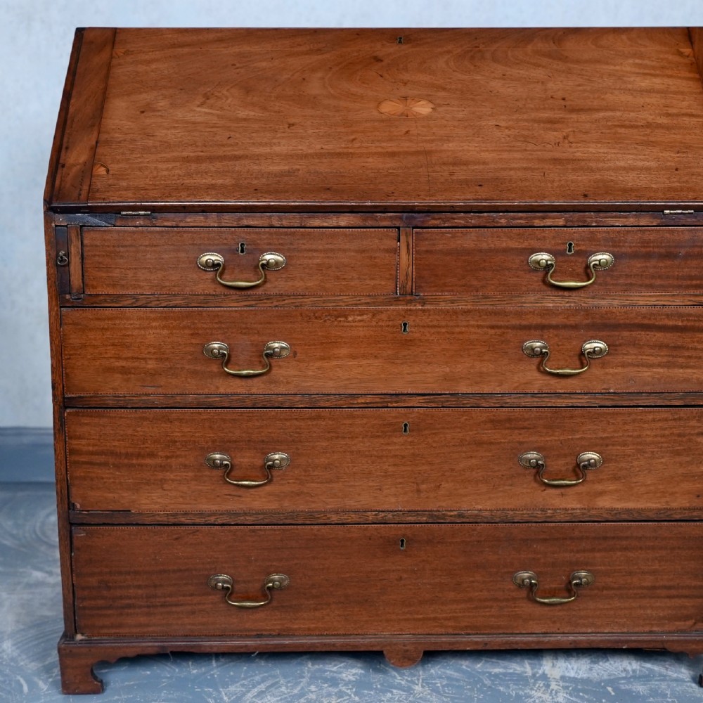 An antique Georgian mahogany writing bureau featuring a slanted fall-front top, four graduated drawers with brass swan-neck handles, and bracket feet. View II