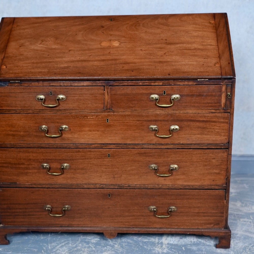 An antique Georgian mahogany writing bureau featuring a slanted fall-front top, four graduated drawers with brass swan-neck handles, and bracket feet. View IV