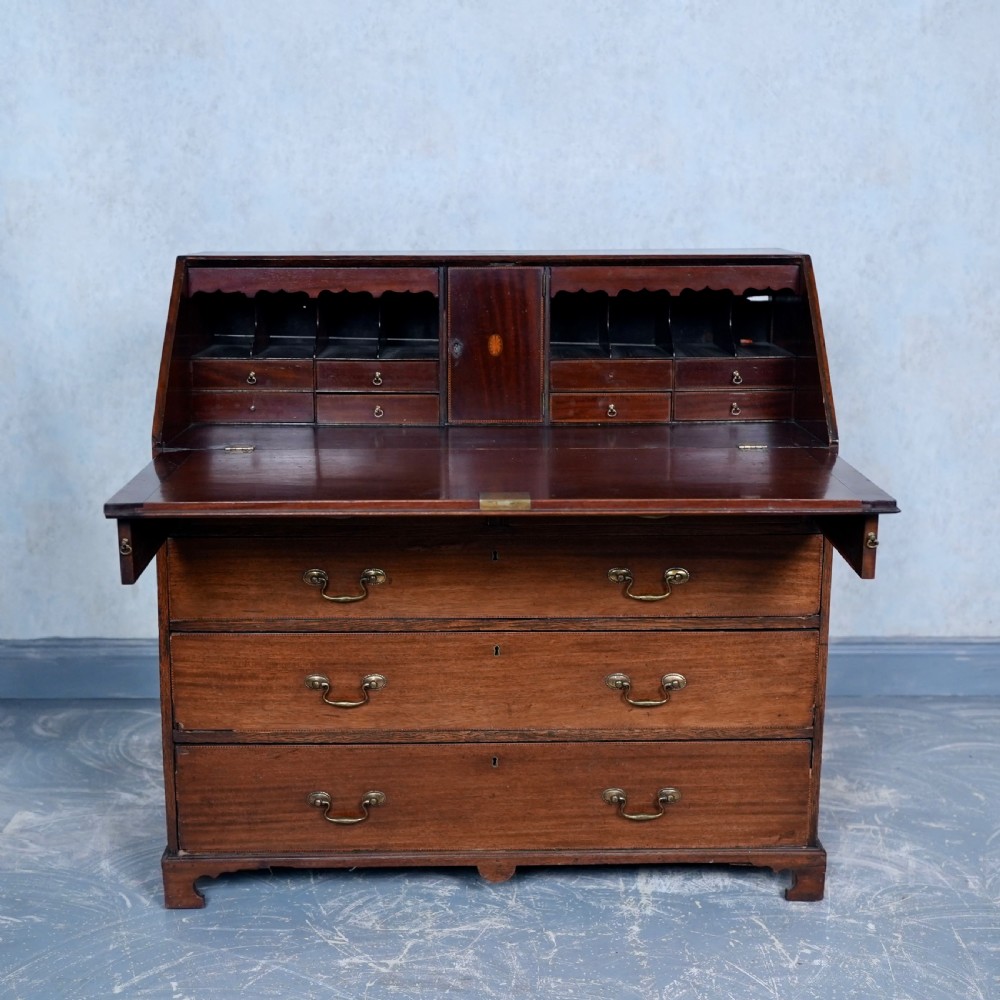 An antique Georgian mahogany writing bureau featuring a slanted fall-front top, four graduated drawers with brass swan-neck handles, and bracket feet. View V