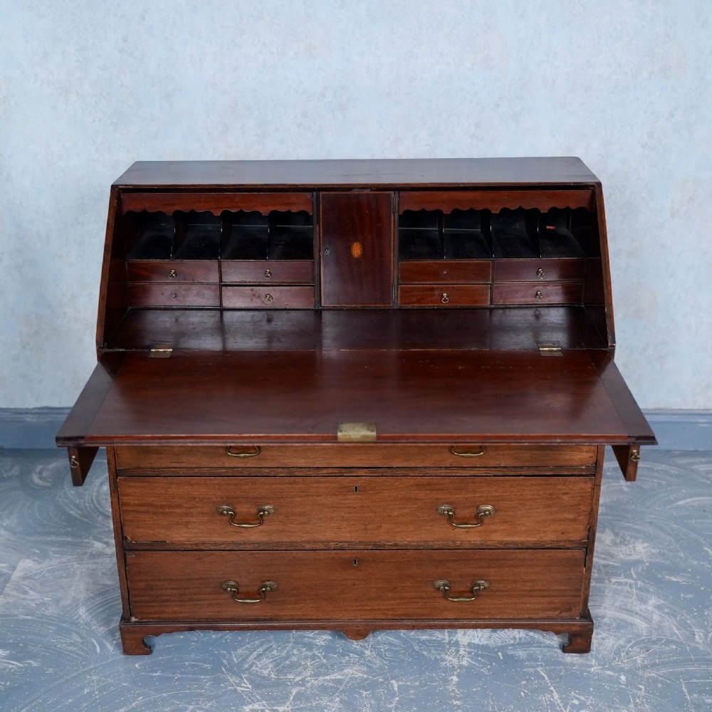 An antique Georgian mahogany writing bureau featuring a slanted fall-front top, four graduated drawers with brass swan-neck handles, and bracket feet. View VI