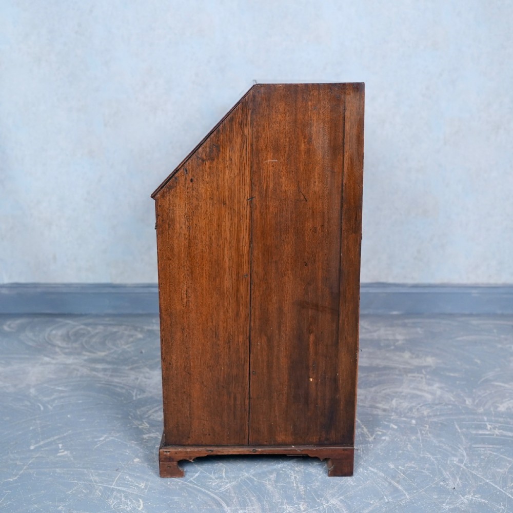 An antique Georgian mahogany writing bureau featuring a slanted fall-front top, four graduated drawers with brass swan-neck handles, and bracket feet. View IX