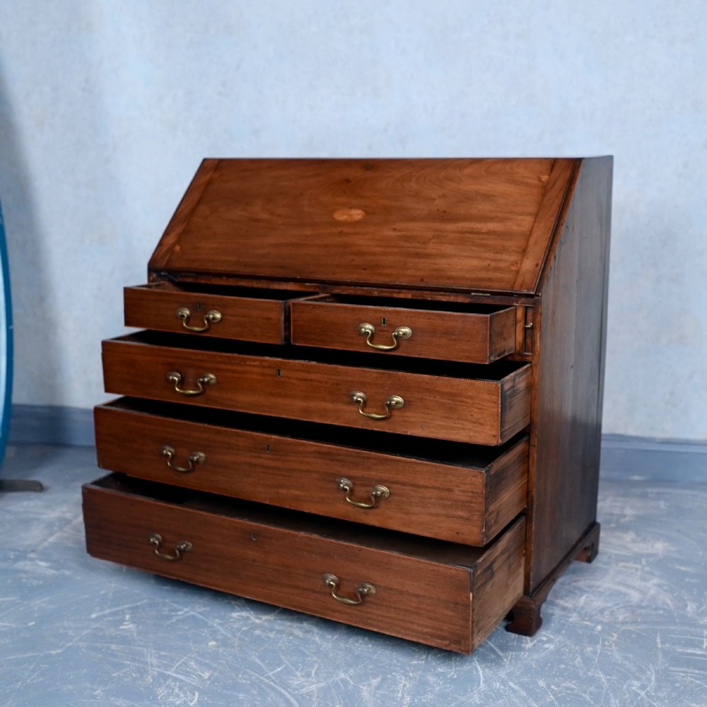 An antique Georgian mahogany writing bureau featuring a slanted fall-front top, four graduated drawers with brass swan-neck handles, and bracket feet. View X