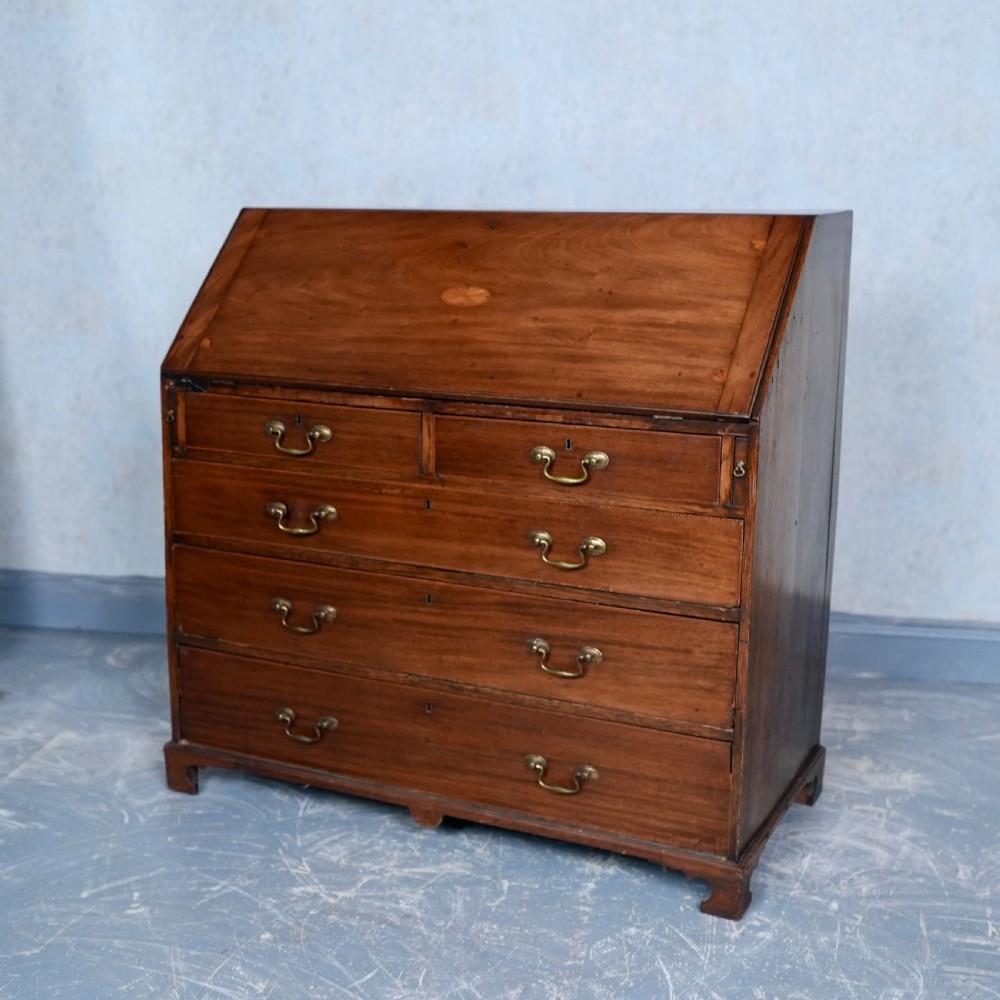 An antique Georgian mahogany writing bureau featuring a slanted fall-front top, four graduated drawers with brass swan-neck handles, and bracket feet. View XI