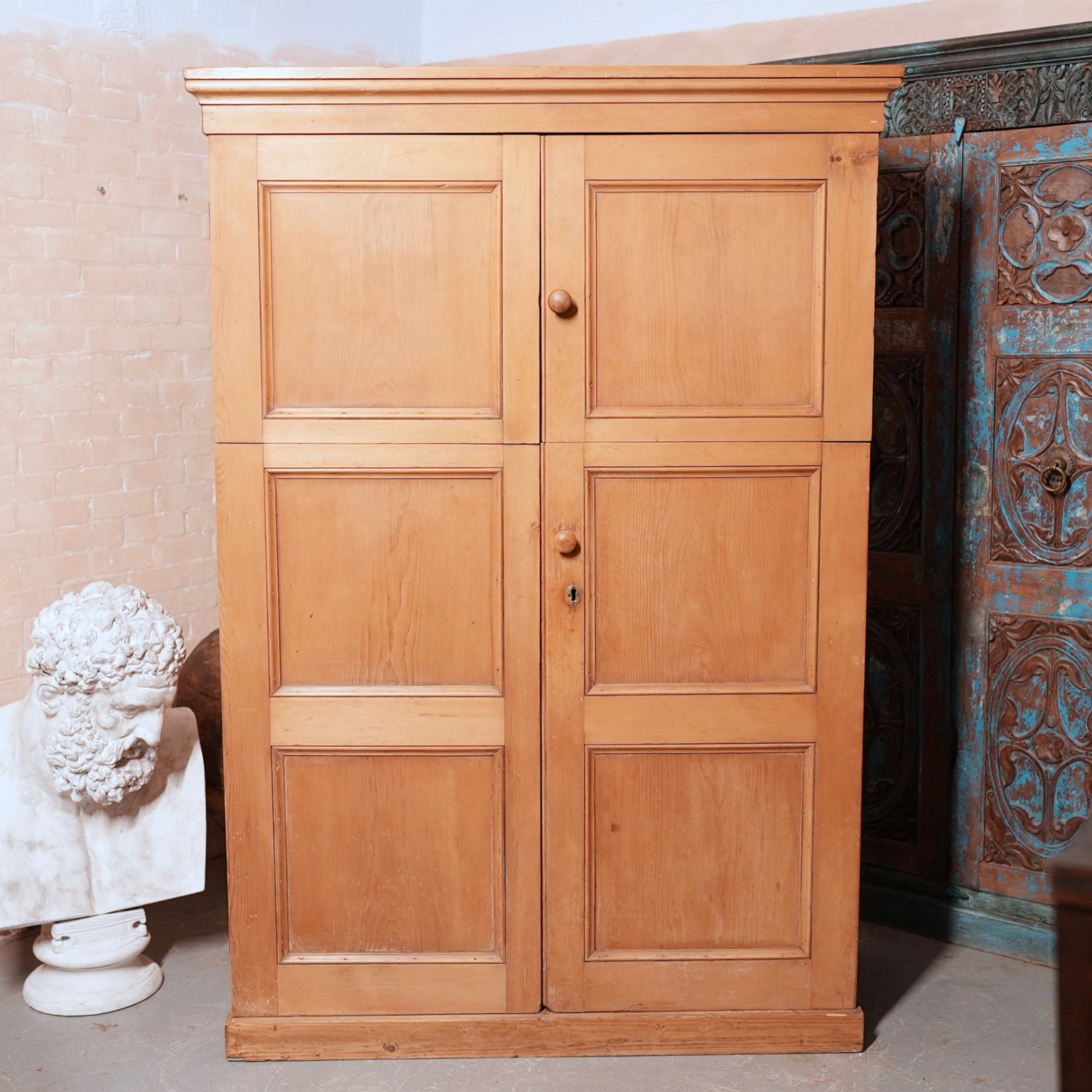 A tall Victorian pine school cupboard with double panelled doors, wooden turn knobs, and a moulded top cornice.