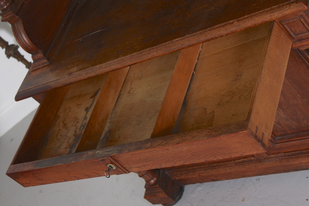 A tall nineteenth-century oak bookcase with a triangular pediment top, two glazed glass doors, a single middle drawer, and a lower double-door cupboard flanked by turned side columns. View IX