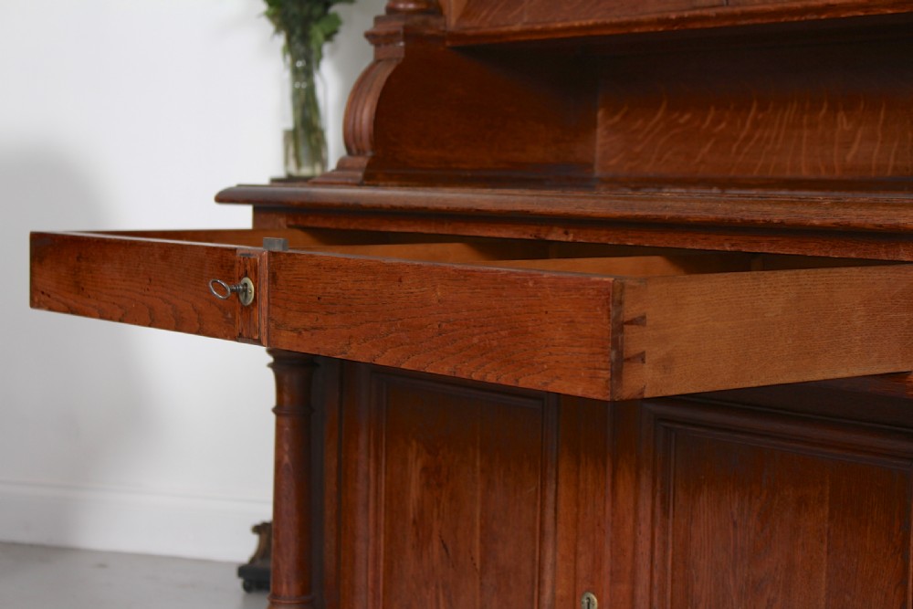 A tall nineteenth-century oak bookcase with a triangular pediment top, two glazed glass doors, a single middle drawer, and a lower double-door cupboard flanked by turned side columns. View X