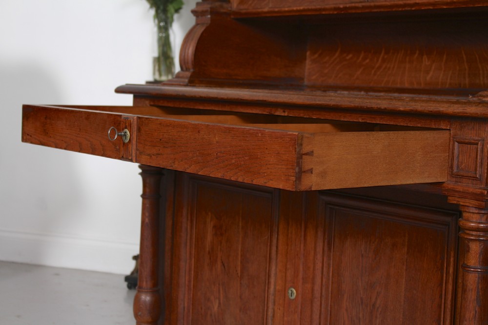 A tall nineteenth-century oak bookcase with a triangular pediment top, two glazed glass doors, a single middle drawer, and a lower double-door cupboard flanked by turned side columns. View XI