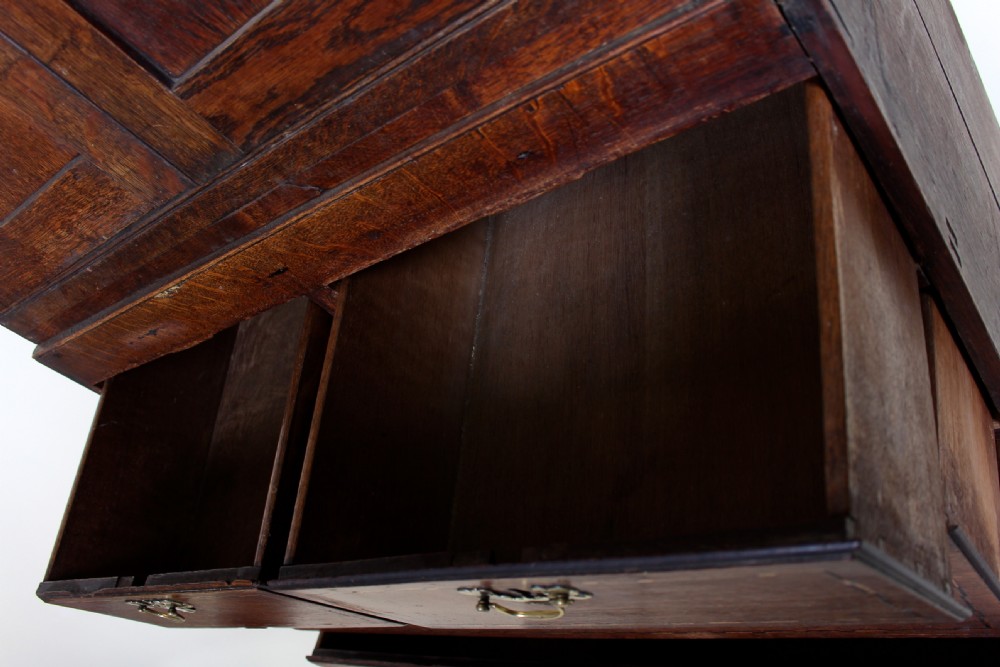 A tall 18th-century Georgian dark oak cupboard featuring panelled upper doors above six drawers with brass drop handles and stringing inlay, resting on turned feet. View XIV