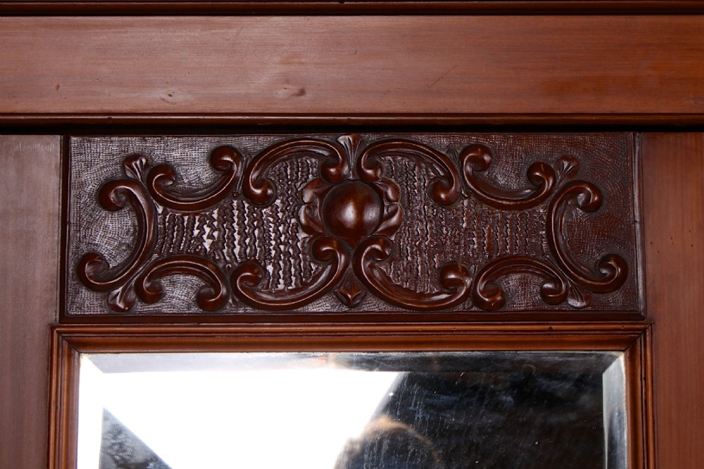 A Victorian triple-door mahogany wardrobe featuring a central mirrored door, carved foliate upper panels, and a solid plinth base. View XI