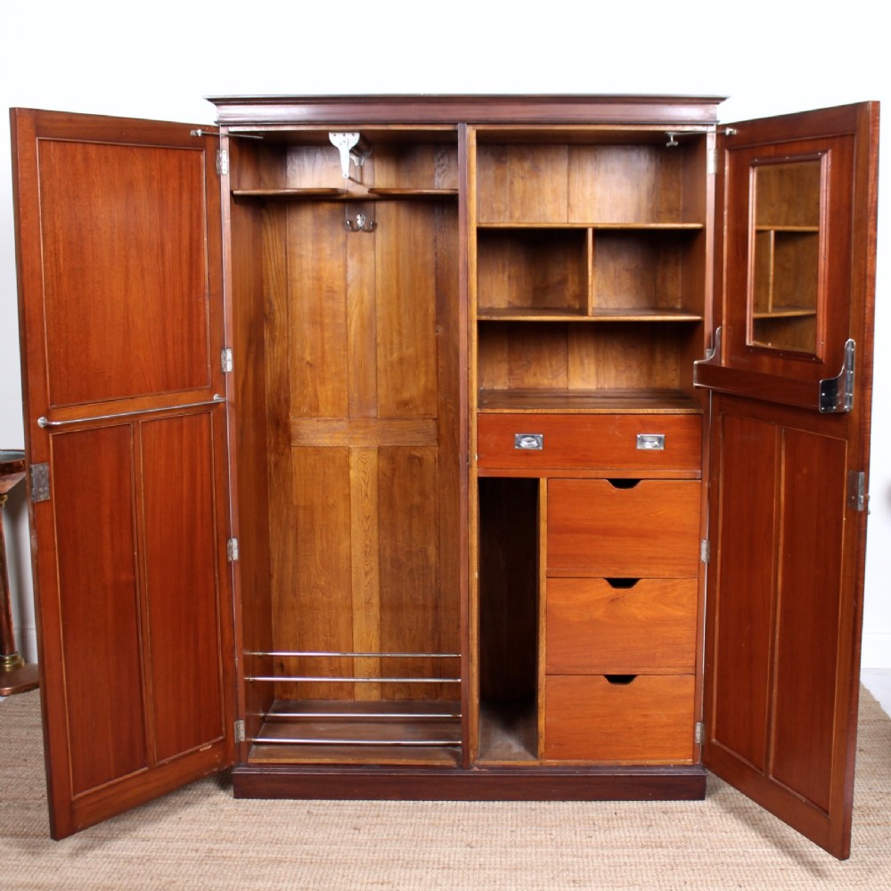 An open Edwardian mahogany compactum wardrobe featuring a full-height hanging compartment on the left and fitted internal shelving, drawers, and an inset mirror on the right.