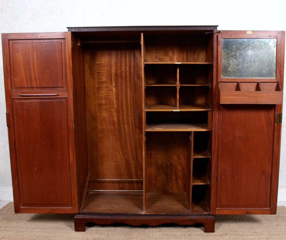 An open Edwardian mahogany compactum wardrobe displaying internal hanging space, fitted shelves, small compartments, and an interior door mirror.