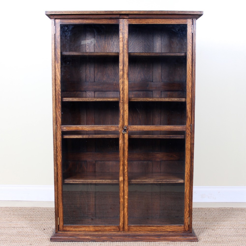 An Edwardian warm brown oak bookcase featuring twin full-length glazed glass doors and interior wooden shelves.