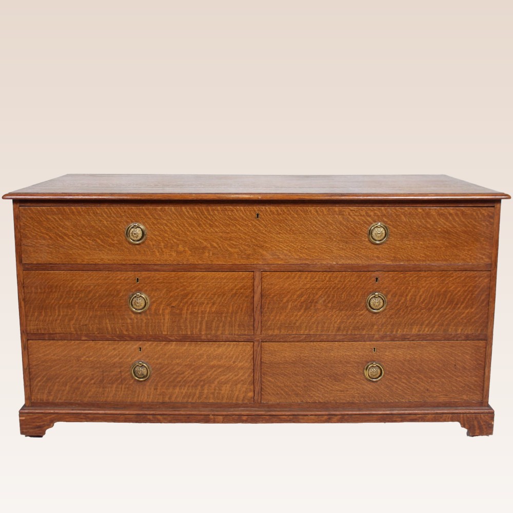 A wide antique oak chest of drawers featuring five drawers with brass ring handles resting on bracket feet.