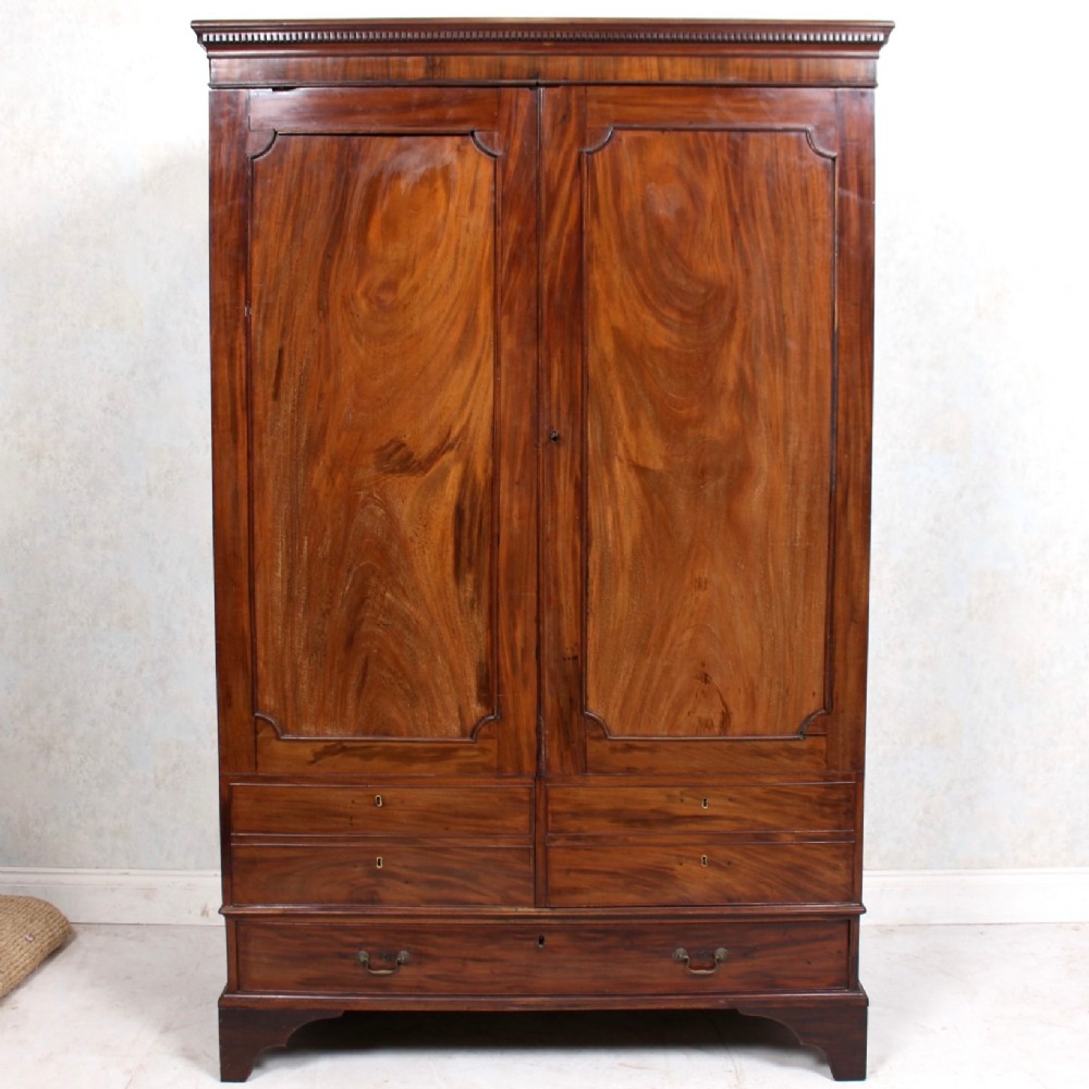 A tall 19th-century mahogany wardrobe featuring flame veneer double panel doors above lower drawers resting on bracket feet.