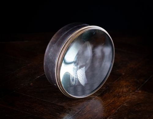 fig 1. A Victorian cylindrical desktop magnifier featuring a thick circular glass convex lens set within a heavy metal rim.