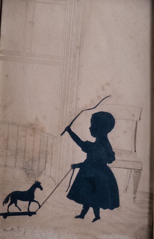 fig 1. A 19th-century cut-paper silhouette depicting a young child pulling a toy horse on wheels, set within a bevelled wooden frame with a gilded inner slip.