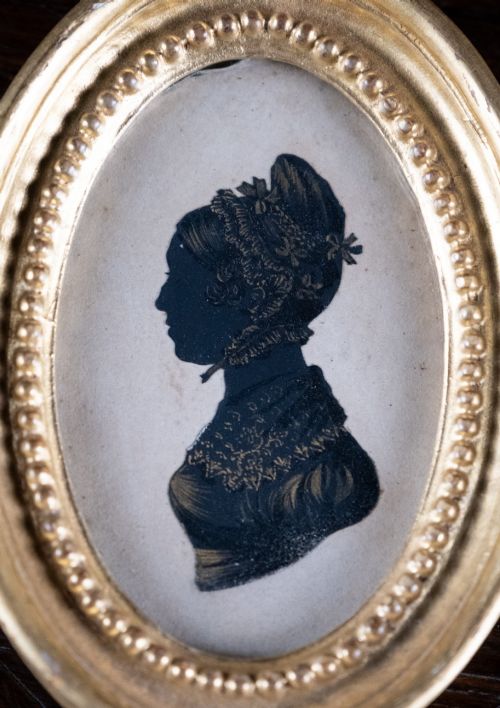 fig 1. An oval framed Regency-era miniature silhouette depicting the profile of a lady embellished with fine gold detailing, set within a beaded gilt frame.