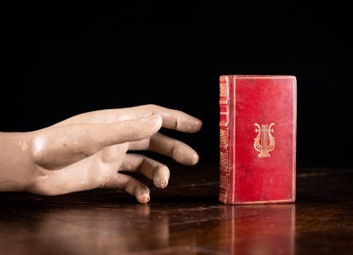 fig 1. An 1821 miniature book bound in red leather featuring gilt spine tooling, raised bands, and gold lettering.